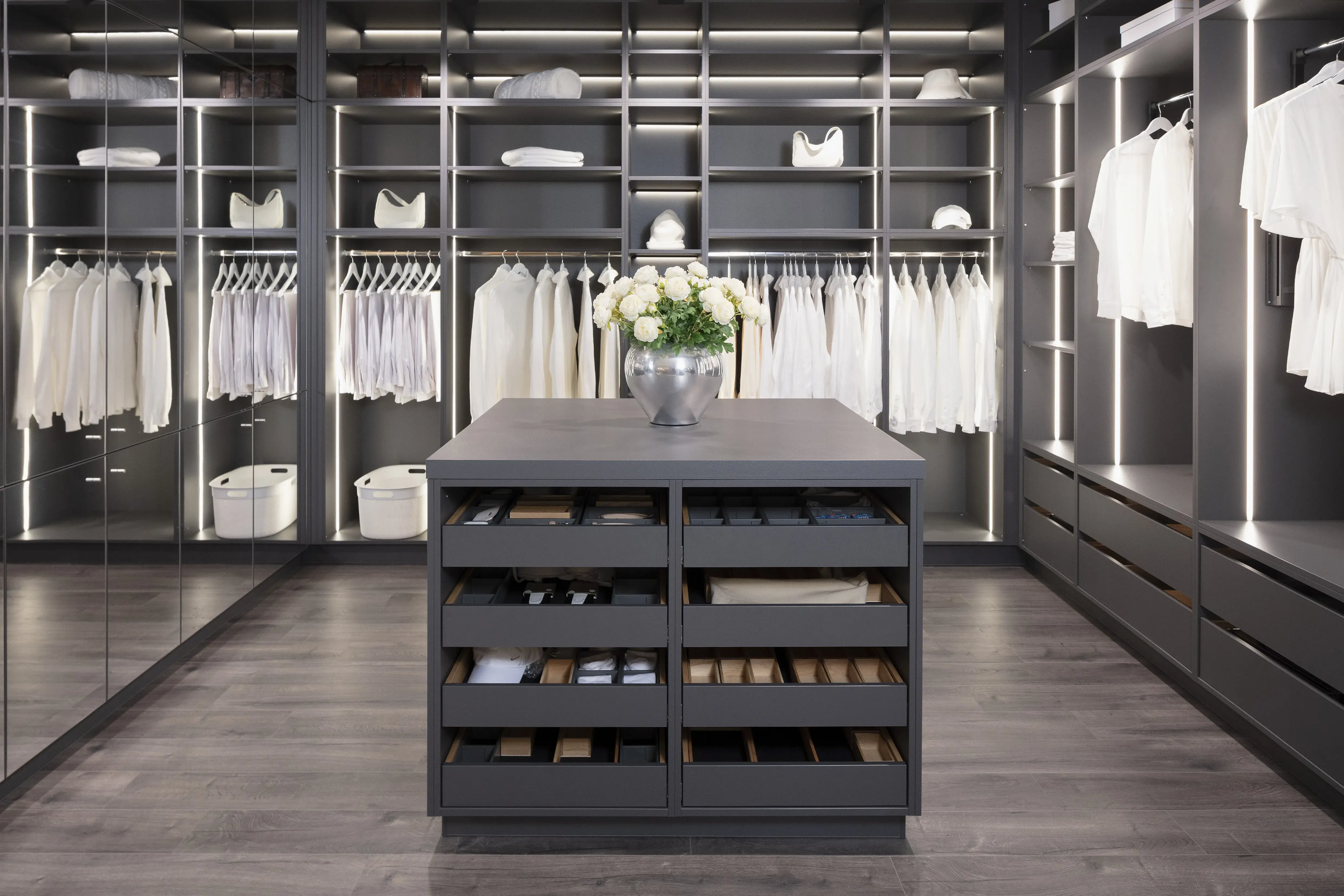 Moderner begehbarer Kleiderschrank mit weißen Hemden und Blumenstrauß auf Mittelinsel.